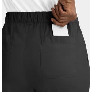 A close-up of a woman holding a white phone in the back pocket of black cargo pants with an elastic waistband.