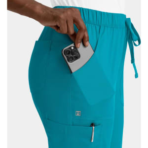 A pair of turquoise women's cargo pants featuring a full elastic waistband and side pockets, with a phone partially visible.