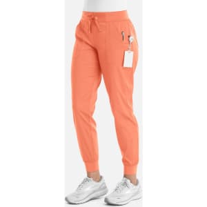 An orange pair of jogger pants with a drawstring waist and zippered pockets, displayed on a model wearing grey shoes.