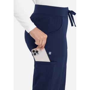 A pair of navy women's jogger-style pants featuring side pockets and a waistband tie, with a phone being placed in a pocket.