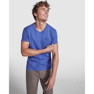 A blue T-shirt with short sleeves and a pocket, worn by a smiling man in casual attire.