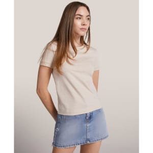 A light beige women's T-shirt with short sleeves, paired with a denim mini skirt. The shirt features a subtle logo.