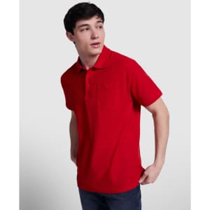 A red polo shirt featuring a collar and a chest pocket, modelled by a young man with a neutral background.