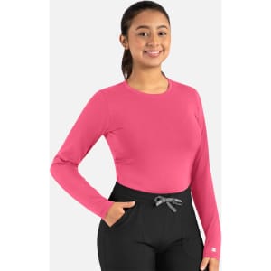 A pink long-sleeve underscrub tee with a fitted design and a logo on the sleeve, paired with black pants.