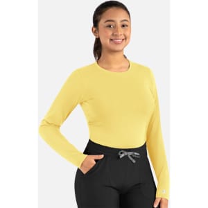 A long-sleeve underscrub tee in bright yellow, paired with black pants. The model is smiling and has a logo on the tee.