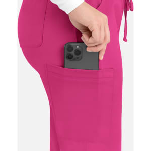 A close-up of bright pink cargo pants with a phone being placed into a back pocket. The pants feature a logo.