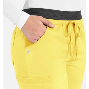 A close-up of yellow cargo pants featuring a black elastic waistband, side pockets, and a small logo.