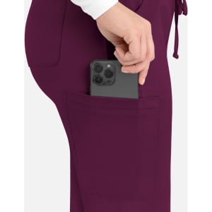 A woman inserting a smartphone into the pocket of purple cargo pants. The pants have a drawstring waist and a logo.