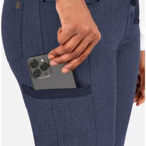 A close-up of a hand placing a smartphone into a navy tapered pant pocket. The pants feature a sleek design.