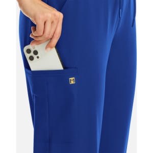 A close-up of a hand holding a smartphone in the pocket of blue joggers, featuring a small logo.