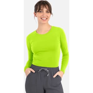 A woman is wearing a bright lime green long-sleeve tee paired with grey pants. The tee features a logo.