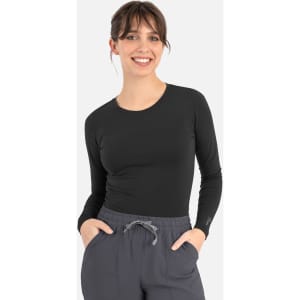 A fitted black long-sleeve underscrub tee worn by a model, paired with grey pants. The product features a logo.