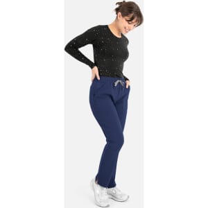 A woman in a black long-sleeve top and navy blue pants, smiling while standing with her hands in her pockets.