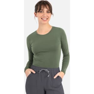 A woman wearing a long-sleeve green underscrub tee paired with grey pants. The tee features a logo.