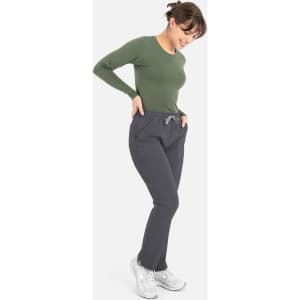 A model in a green long-sleeve underscrub tee and grey pants, featuring a branded logo on the tee.
