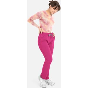 A woman wearing a tie-dye pink and orange long-sleeve tee with pink pants, posed smiling downwards.