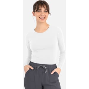 A white long-sleeve underscrub tee, paired with grey pants, displayed on a smiling model.