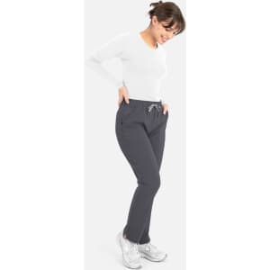 A woman wearing a white long-sleeve underscrub tee and grey pants, smiling with hands in pockets.