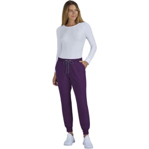 A woman wearing a fitted white long-sleeve top and purple jogger pants, with a drawstring at the waist.