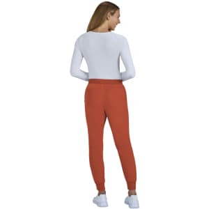 A pair of rust-coloured jogger pants displayed on a model wearing a white top, with a logo visible on the pants.
