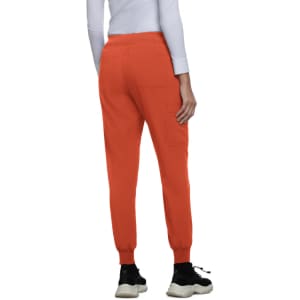 An orange jogger with elastic cuffs and back pockets, worn by a person facing away. Features a logo.