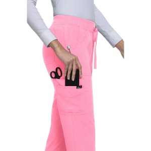A pair of pink jogger pants with pockets, one holding scissors and a phone. The pants have a logo.