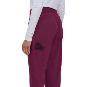 A pair of burgundy jogger pants with a scissors tucked into the side pocket, worn by a person facing away.