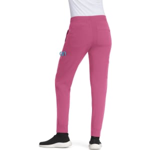 A pair of pink jogger pants with pockets, featuring a logo on the left side and styled with black shoes.