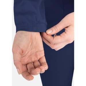 A close-up of a person's hand adjusting the cuff of a navy blue round neck jacket, featuring a logo.