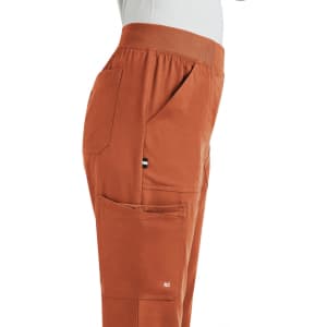 A side view of orange boot cut pants featuring pockets and an elastic waistband. The garment includes a small logo.