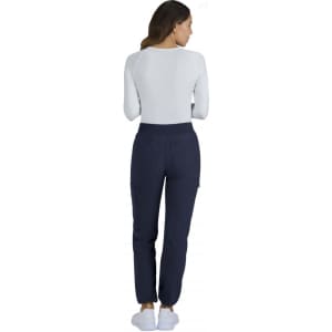 A woman wearing navy Harper Pants, viewed from the back, paired with a white long-sleeve top and slippers.
