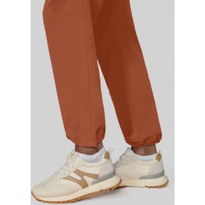 Wide leg pants in a rich terracotta hue, paired with cream and beige sneakers, displayed against a neutral background.