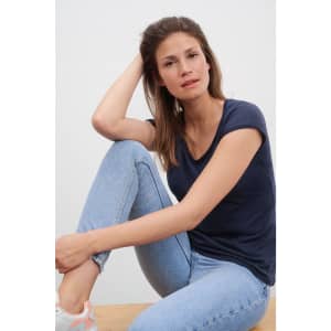 A navy blue ladies' t-shirt featuring a scoop neckline, paired with light blue jeans and a natural backdrop.