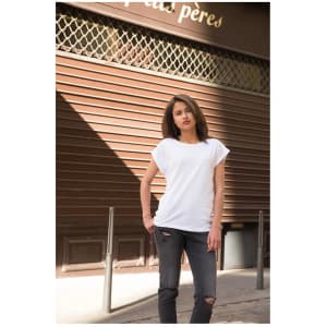 A model wearing a white casual T-shirt paired with distressed black jeans, standing in an urban setting.