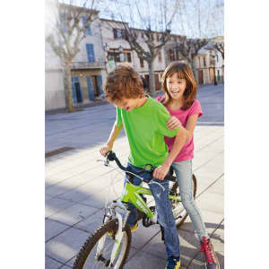 A boy in a green T-shirt rides a bike while a girl in a pink T-shirt smiles behind him.