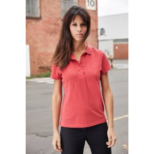 A red ladies' polo shirt with a collar and buttons, modelled by a woman in an outdoor setting.