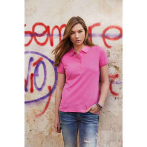 A pink ladies polo shirt featuring a collar, worn by a model against a graffiti background. The shirt has a logo.