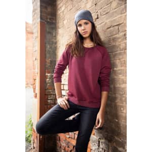 A maroon jumper with long sleeves worn by a model, paired with a grey beanie, set against a brick wall.