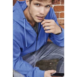A blue men's zip hoodie is worn by a man sitting against a brick wall, holding a smartphone.