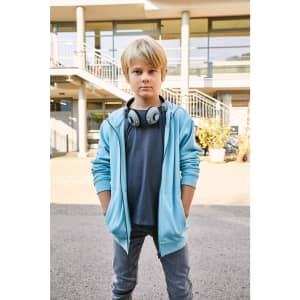 A child in a light blue zip hoodie with headphones, standing confidently outdoors in a casual setting.