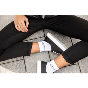 Organic sneaker socks in white, worn with black sneakers and black cropped pants on a grey tiled surface.