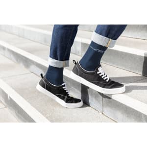 A pair of navy organic socks worn with black shoes, standing on outdoor steps with rolled-up denim jeans.