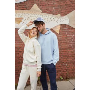 A cream and blue hoodie worn by a man and woman, smiling in front of a brick wall with a fish mural.