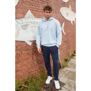 A model wearing a light blue men's lounge hoodie paired with navy pants, standing against a brick wall.