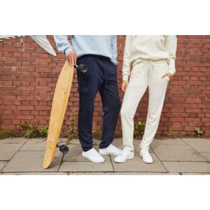 A pair of lounge pants in navy and cream, paired with casual white shoes and a skateboard, set against a brick wall.