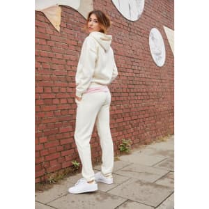 Cream-coloured lounge pants paired with a matching hoodie, set against a brick wall backdrop.
