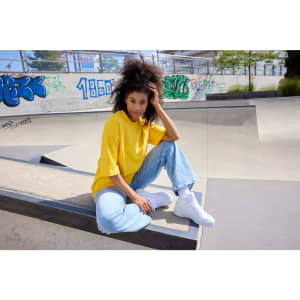 A yellow oversized T-shirt paired with light blue jeans, worn by a person sitting at a skate park.