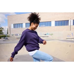 A purple oversized sweatshirt with a relaxed fit, worn by a person smiling near a skate park.