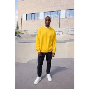 A person wearing an oversized yellow sweatshirt and black trousers stands in an outdoor skate park.