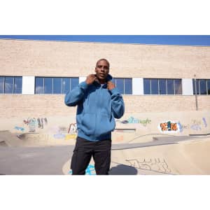 An oversized hooded jacket in blue, worn by a person standing in a skate park with graffiti on the walls.
